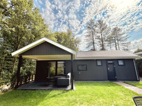 Bos Cottage Deluxe en De Thijmse Berg, Países Bajos, cabaña de madera oscura con terraza cubierta.