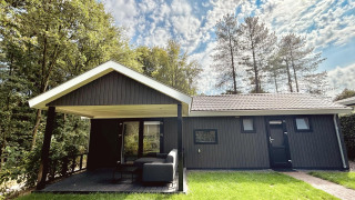 Bos Cottage Deluxe a De Thijmse Berg nei Paesi Bassi, lodge in legno scuro con terrazza coperta.