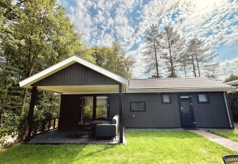 Bos Cottage Deluxe bei De Thijmse Berg, Niederlande, schwarze Holzlodge vor Bäumen und Himmel.