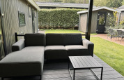 Udendørs loungeområde med grå sofa og bord på træterrasse ved en moderne lodge i Bos Cottage Deluxe, Holland.