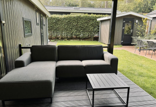 Zona de estar exterior con sofá gris y mesa en la terraza de una cabaña Bos Cottage Deluxe en los Países Bajos.