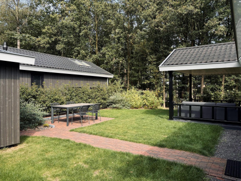 Acogedora terraza con mesa y sillas en Bos Cottage Deluxe de De Thijmse Berg, rodeada de vegetación en Países Bajos.