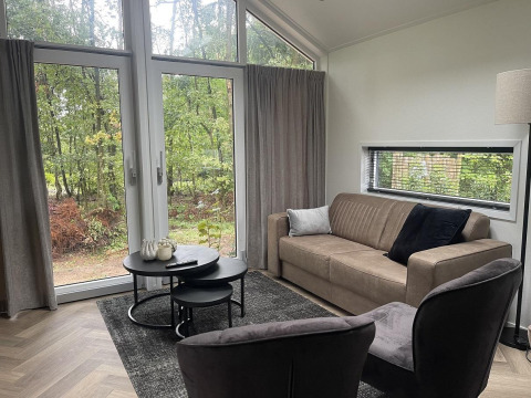 Sala de estar en Bos Cottage Deluxe, De Thijmse Berg, Países Bajos, con grandes ventanales y decoración moderna.
