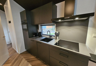 Cocina moderna con armarios oscuros y suelo de madera en Bos Cottage Deluxe, De Thijmse Berg, Países Bajos