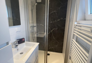 Baño moderno y compacto con ducha, lavabo blanco y radiador de toallas en Bos Cottage Deluxe, Países Bajos.