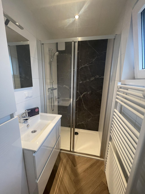 Moderne, compacte badkamer met douche, witte lavabo en handdoekradiator bij Bos Cottage Deluxe, Nederland.