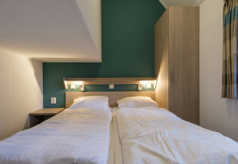 Gemütliches Schlafzimmer in der Vechtdallodge, Kampeerdorp de Zandstuve, mit zwei Einzelbetten und grünem Akzent.