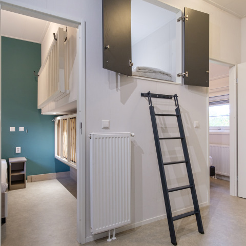 Interior de un lodge moderno con cama alta, escalera y zonas de descanso en Kampeerdorp de Zandstuve, Países Bajos.