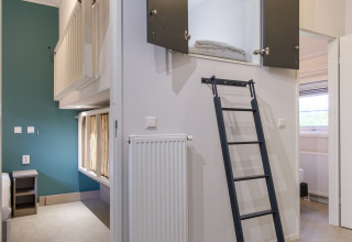 Interior de un lodge moderno con cama alta, escalera y zonas de descanso en Kampeerdorp de Zandstuve, Países Bajos.