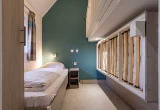Moderne slaapkamer in Vechtdallodge bij Kampeerdorp de Zandstuve, Nederland, met eenpersoonsbedden en groene muur.