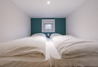 Dormitorio minimalista con dos camas individuales, ropa de cama blanca y pequeña ventana en Vechtdallodge, Países Bajos.