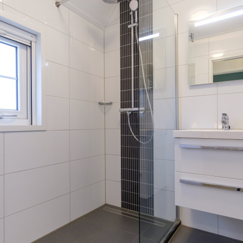 Moderne badeværelse med brusebad, glaspanel, hvidt vaskeskab og vindue i Vechtdallodge, Nederlandene.