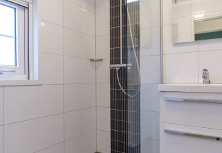 Modern bathroom with shower, glass panel, white sink cabinet and window at Vechtdallodge, Netherlands.