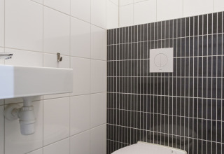 Moderne toilet og håndvask med hvide og mørke fliser i Vechtdallodge, Kampeerdorp de Zandstuve, Holland.