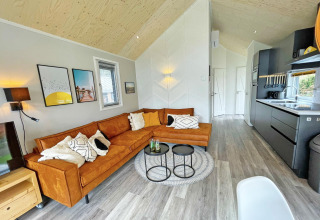 Sala moderna en Eco Cottage en De Thijmse Berg, Países Bajos, con sofá naranja y cocina abierta.