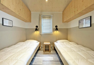 Camera luminosa all’Eco Cottage a De Thijmse Berg, Paesi Bassi, con due letti singoli e arredo in legno chiaro.