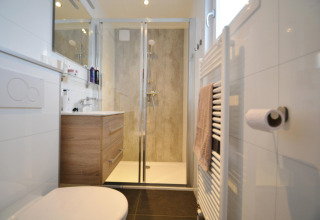 Baño moderno con ducha de vidrio, tocador de madera y toallero en la Eco Cottage en De Thijmse Berg.