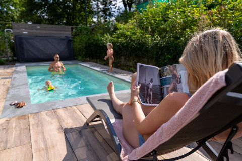 Familia se relaja junto a la piscina en Pool Lodge de De Thijmse Berg, Países Bajos, mujer lee revista.