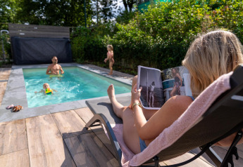 Familia se relaja junto a la piscina en Pool Lodge de De Thijmse Berg, Países Bajos, mujer lee revista.