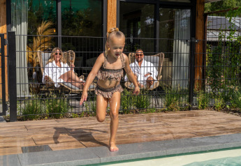 Bambina gioca vicino alla piscina mentre due adulti si rilassano in terrazza al Pool Lodge a De Thijmse Berg, Paesi Bassi.