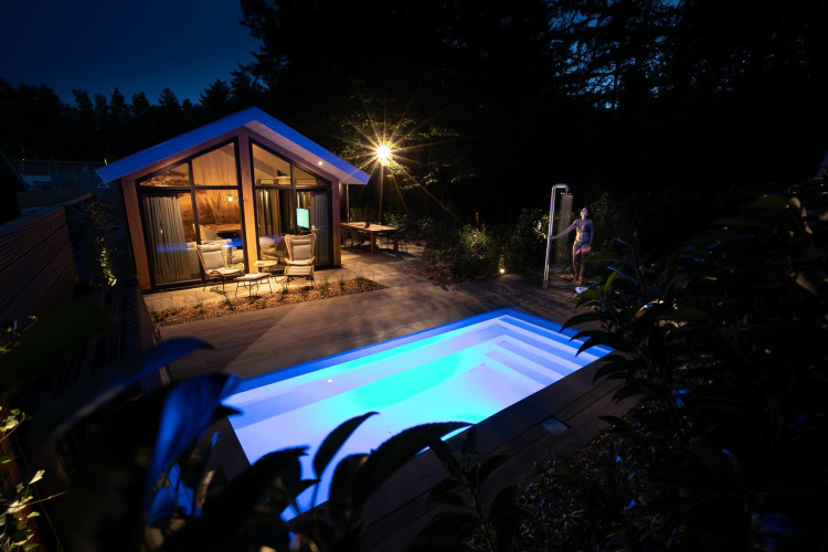 Abendaufnahme der Pool Lodge in De Thijmse Berg, Niederlande, mit beleuchtetem Pool und Terrasse.