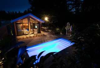 Avondzicht op Pool Lodge bij De Thijmse Berg, Nederland, met verlicht zwembad en gezellige patio.