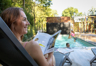 Vrouw leest bij zwembad Pool Lodge, De Thijmse Berg, terwijl kinderen in water spelen, Nederland.