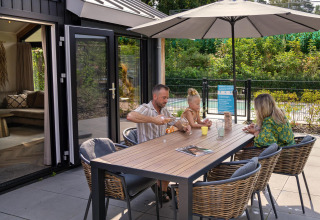 Familia disfruta de una comida y juegos al aire libre bajo una sombrilla en Pool Lodge, De Thijmse Berg, Países Bajos.