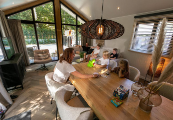 Familie hygger sig indendørs i Pool Lodge på De Thijmse Berg, Holland, med spil ved spisebordet.
