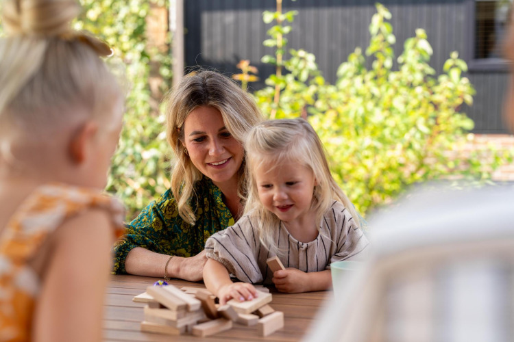 Eine Mutter spielt draußen mit ihren Kindern Jenga am Tisch in der Pool Lodge bei De Thijmse Berg, Niederlande.