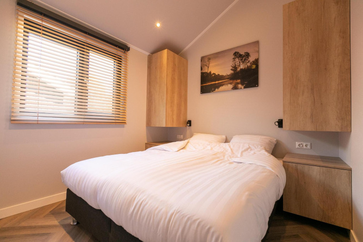 Modernes Schlafzimmer in der Pool Lodge, De Thijmse Berg, Niederlande, mit Holzmöbeln und Fenster.