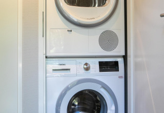 Wasmachine en droogkast gestapeld in Pool Lodge aan de Thijmse Berg, Nederland, in een kleine wasruimte.