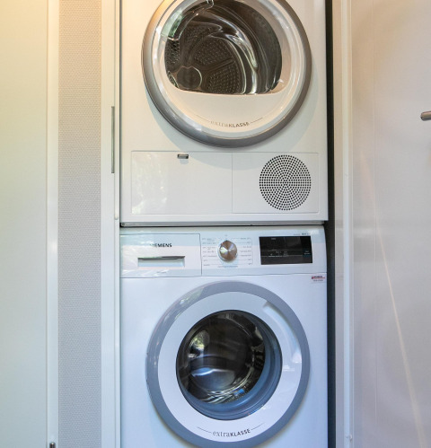 Wasmachine en droogkast gestapeld in Pool Lodge aan de Thijmse Berg, Nederland, in een kleine wasruimte.