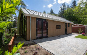 Milieuvriendelijke cottage met houten gevel en groot terras, omringd door bos bij De Thijmse Berg, Nederland.