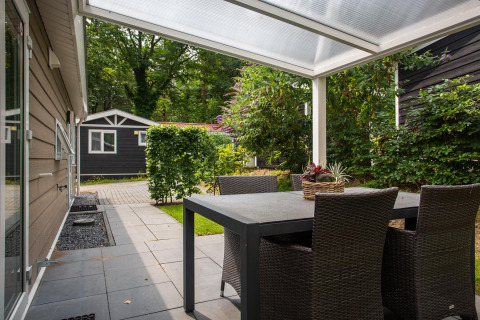 Udendørs terrasse med sort spisebord og stole under en overdækket veranda ved Heuvelrug Cottage Comfort, NL.