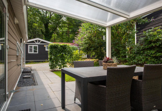 Udendørs terrasse med sort spisebord og stole under en overdækket veranda ved Heuvelrug Cottage Comfort, NL.