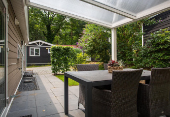 Udendørs terrasse med sort spisebord og stole under en overdækket veranda ved Heuvelrug Cottage Comfort, NL.