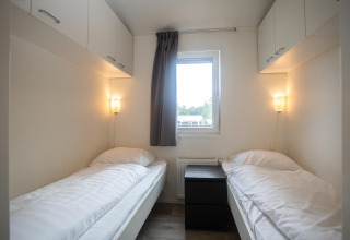 Helles Zimmer mit zwei Einzelbetten, Fenster und Hängeschränken im Heuvelrug Cottage Comfort, Niederlande.