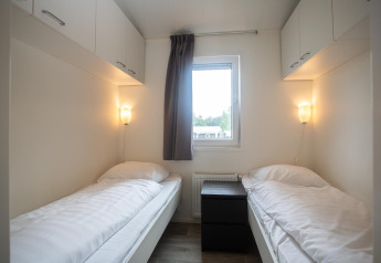 Lyst værelse med to enkeltsenge, et vindue mellem dem og skabe, på Heuvelrug Cottage Comfort, Holland.