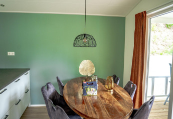 Moderne spisestue i Family Lodge med ovalt bord, grøn væg, sorte stole og udsigt til terrassen.