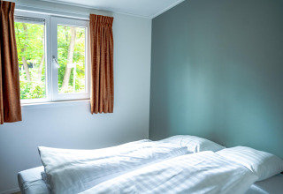 Dormitorio con dos camas individuales, ropa de cama blanca, ventana con cortinas y vista al bosque en De Thijmse Berg.