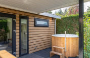 Udendørs hot tub og moderne træfacade på Family Lodge ved De Thijmse Berg i Holland, omgivet af grønne planter.