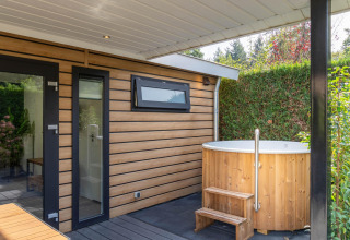 Bain à remous extérieur et façade moderne en bois à la Family Lodge + hot tub, De Thijmse Berg, Pays-Bas, végétation luxuriante.