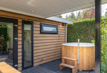 Udendørs hot tub og moderne træfacade på Family Lodge ved De Thijmse Berg i Holland, omgivet af grønne planter.