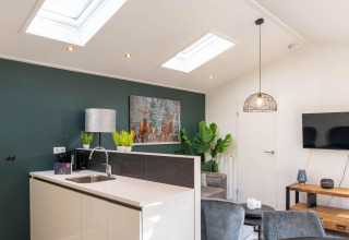 Modern lodge interior with skylights, kitchen, living area, and green plants at De Thijmse Berg, Netherlands.