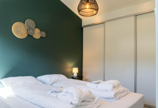 Dormitorio familiar moderno con ropa de cama blanca, pared verde y lámpara en De Thijmse Berg en los Países Bajos.