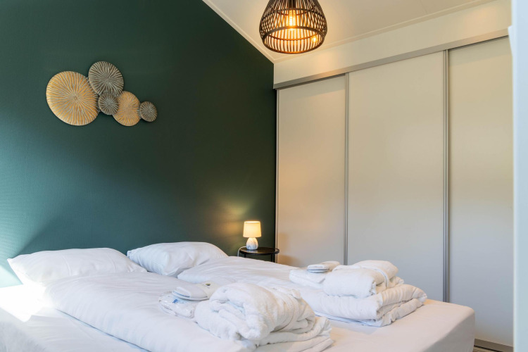Modern family lodge bedroom with white bedding, green accent wall, art decor, and lamp at De Thijmse Berg.