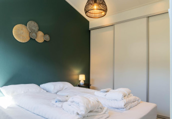 Modern family lodge bedroom with white bedding, green accent wall, art decor, and lamp at De Thijmse Berg.