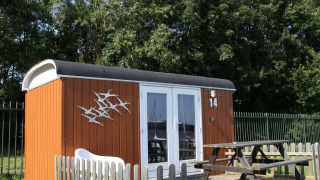 Pequeña casa llamada Tiny Wagons en Marina Parcs Naarden, Países Bajos, con terraza de madera y banco.