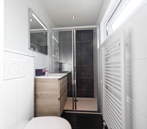 Baño moderno con ducha de vidrio, tocador de madera, espejo y ventana en De Thijmse Berg, Países Bajos.